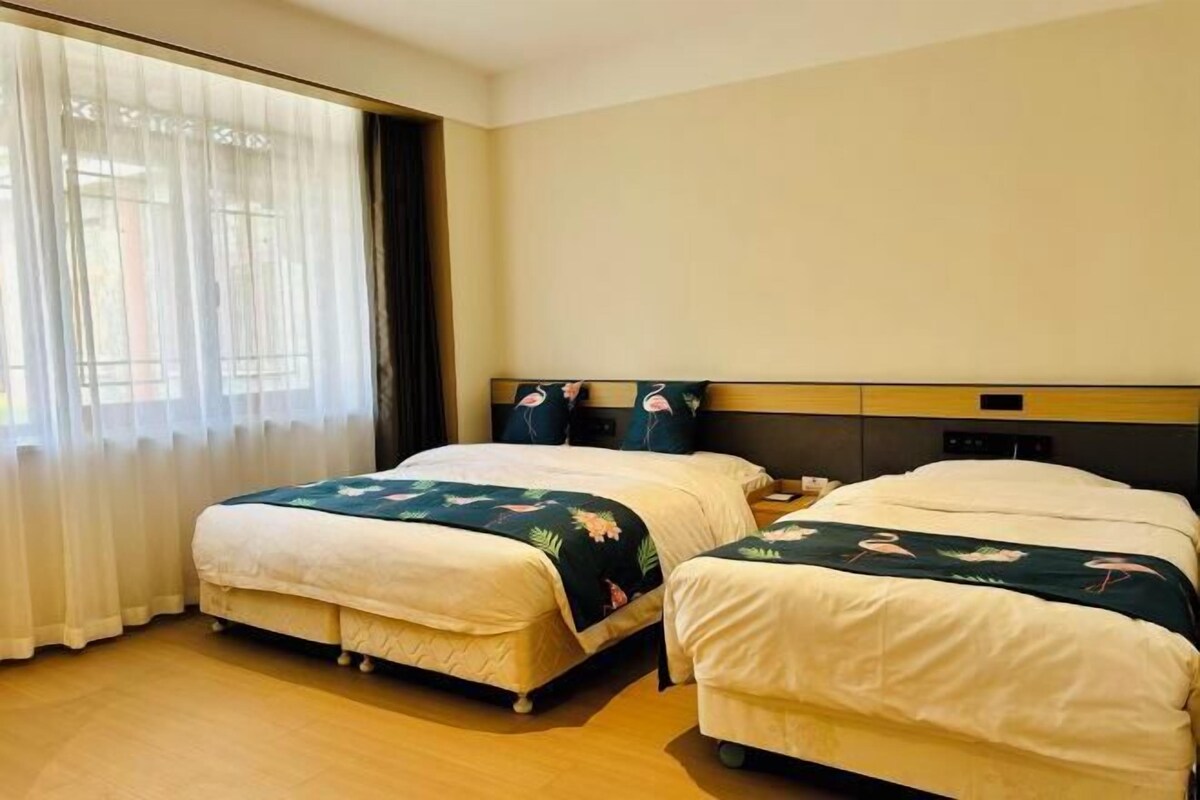 Une chambre d’hôtel avec deux lits, une grande fenêtre avec des rideaux légers et un plancher en bois.