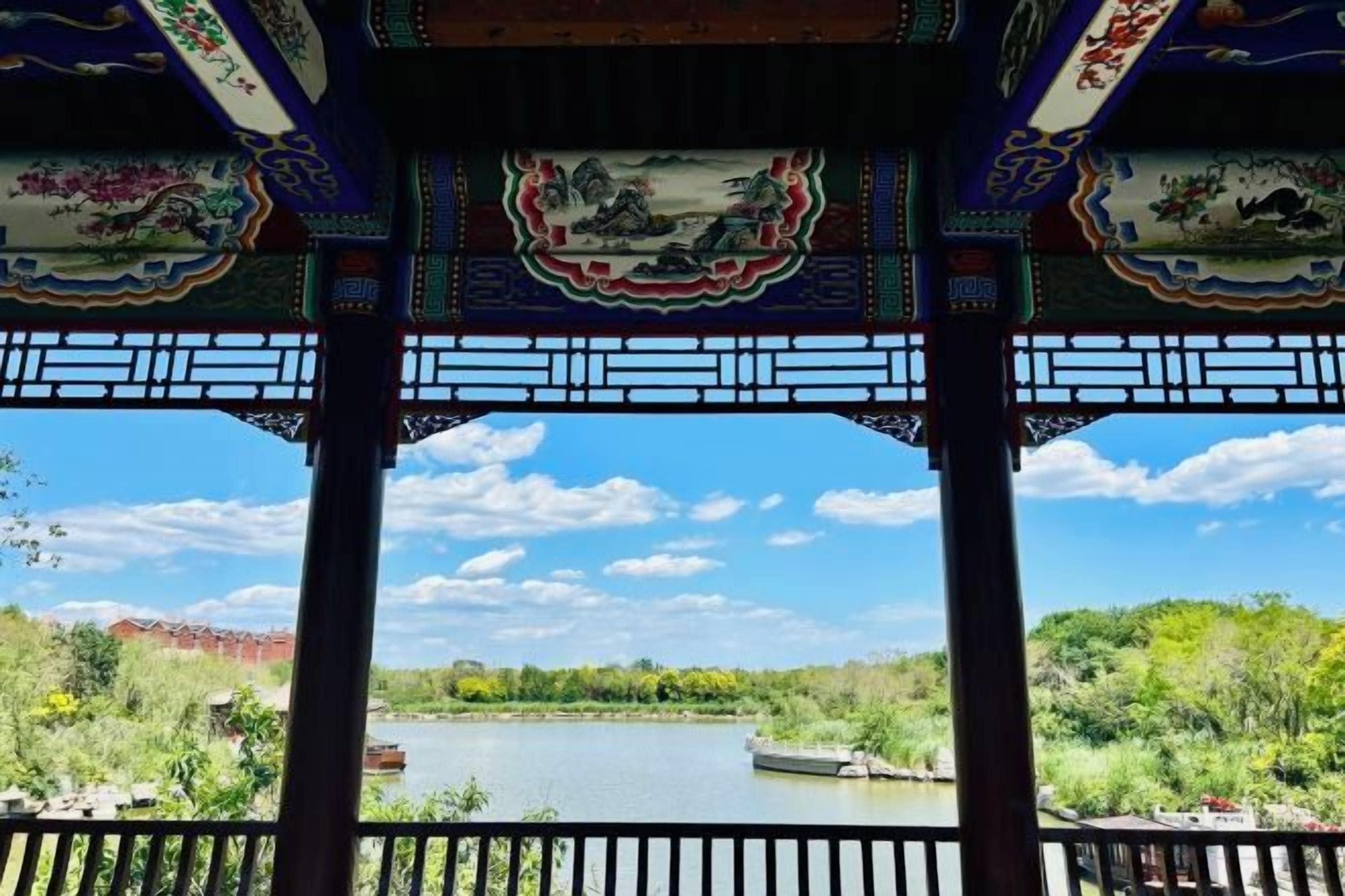 Un pavillon présentant des éléments d’architecture chinoise traditionnelle, avec vue sur un lac et des bateaux.