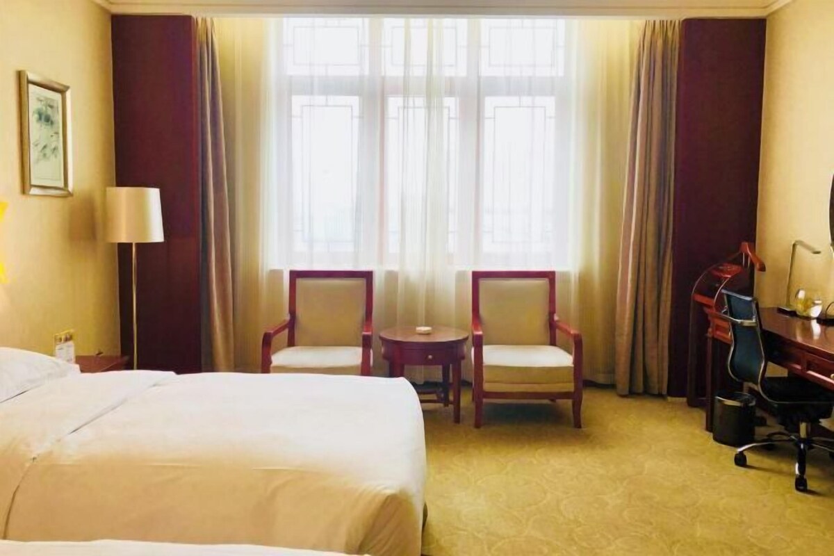 Une chambre d’hôtel avec un lit, deux chaises, un bureau et une lampe.