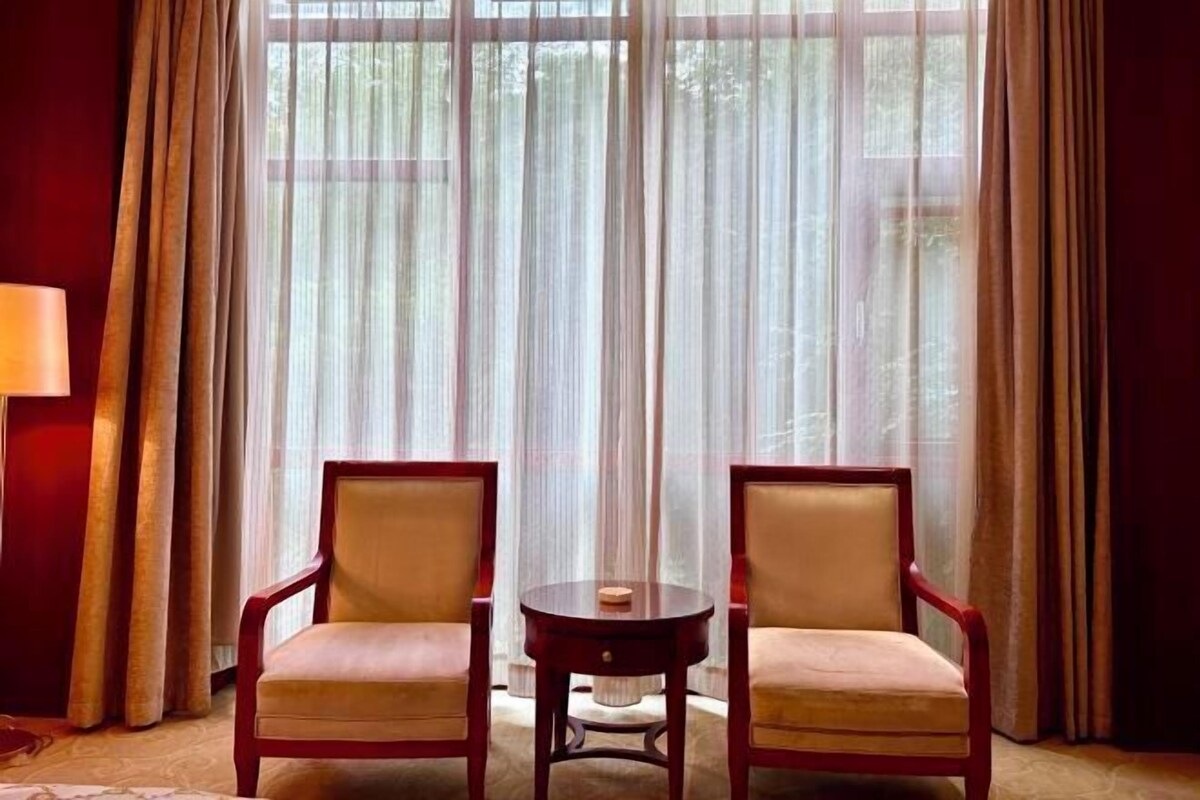 Une pièce avec deux chaises, une petite table ronde et des rideaux légers.