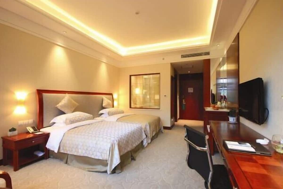 A hotel room with two beds, a desk, a chair, a TV, and a door leading to a bathroom.