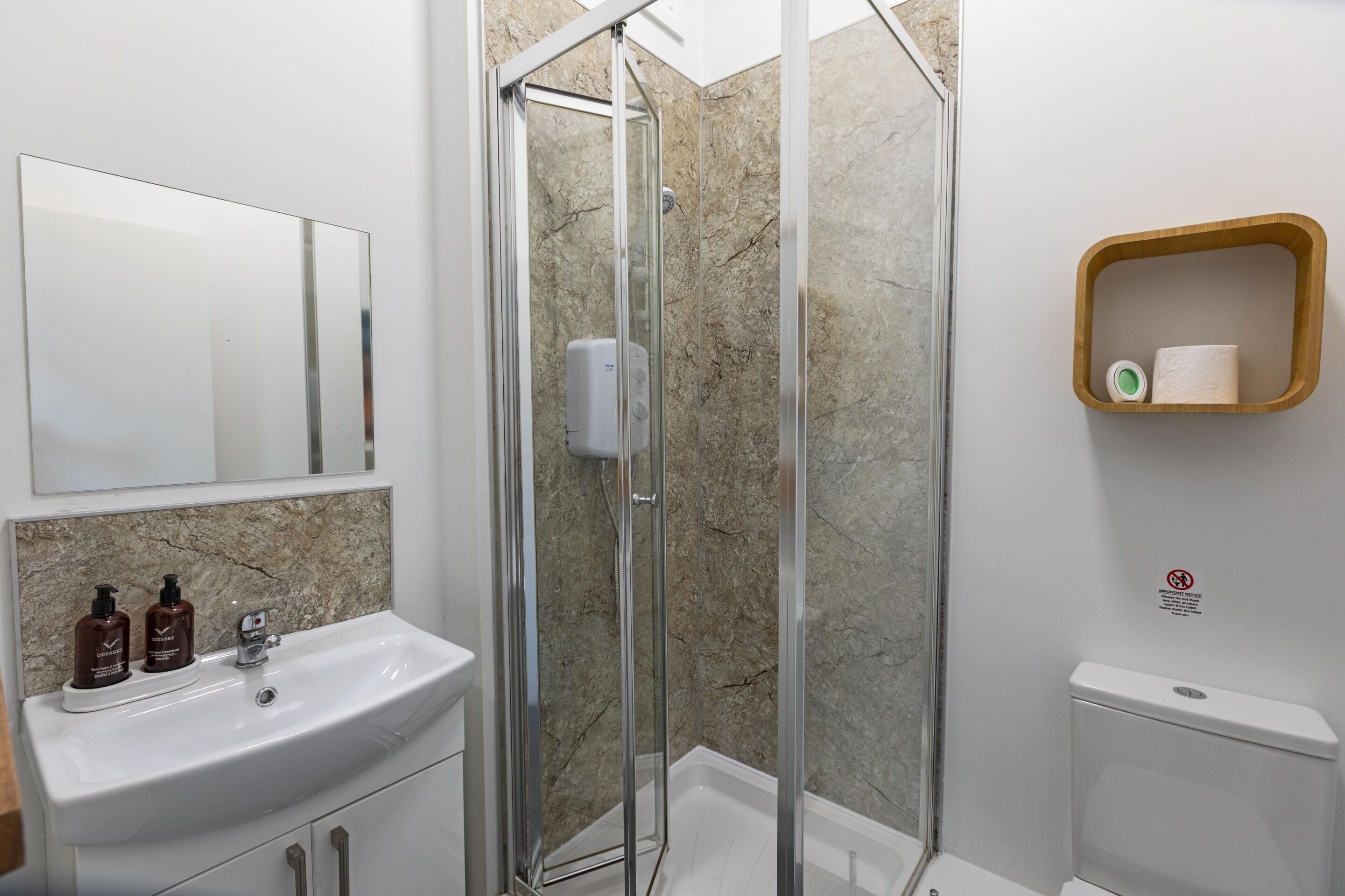 A bathroom with a glass-enclosed shower, a sink with toiletries, and a toilet.