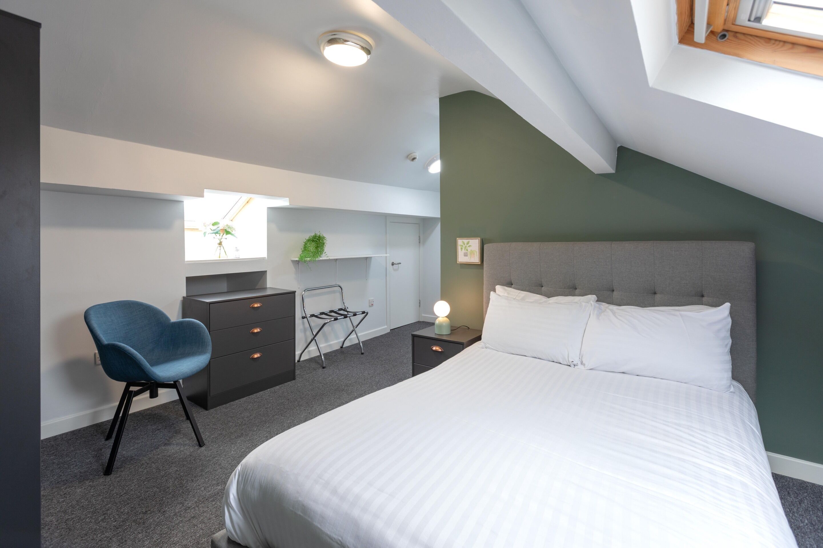 A bedroom with a bed, a chair, a dresser, a nightstand, and a window.
