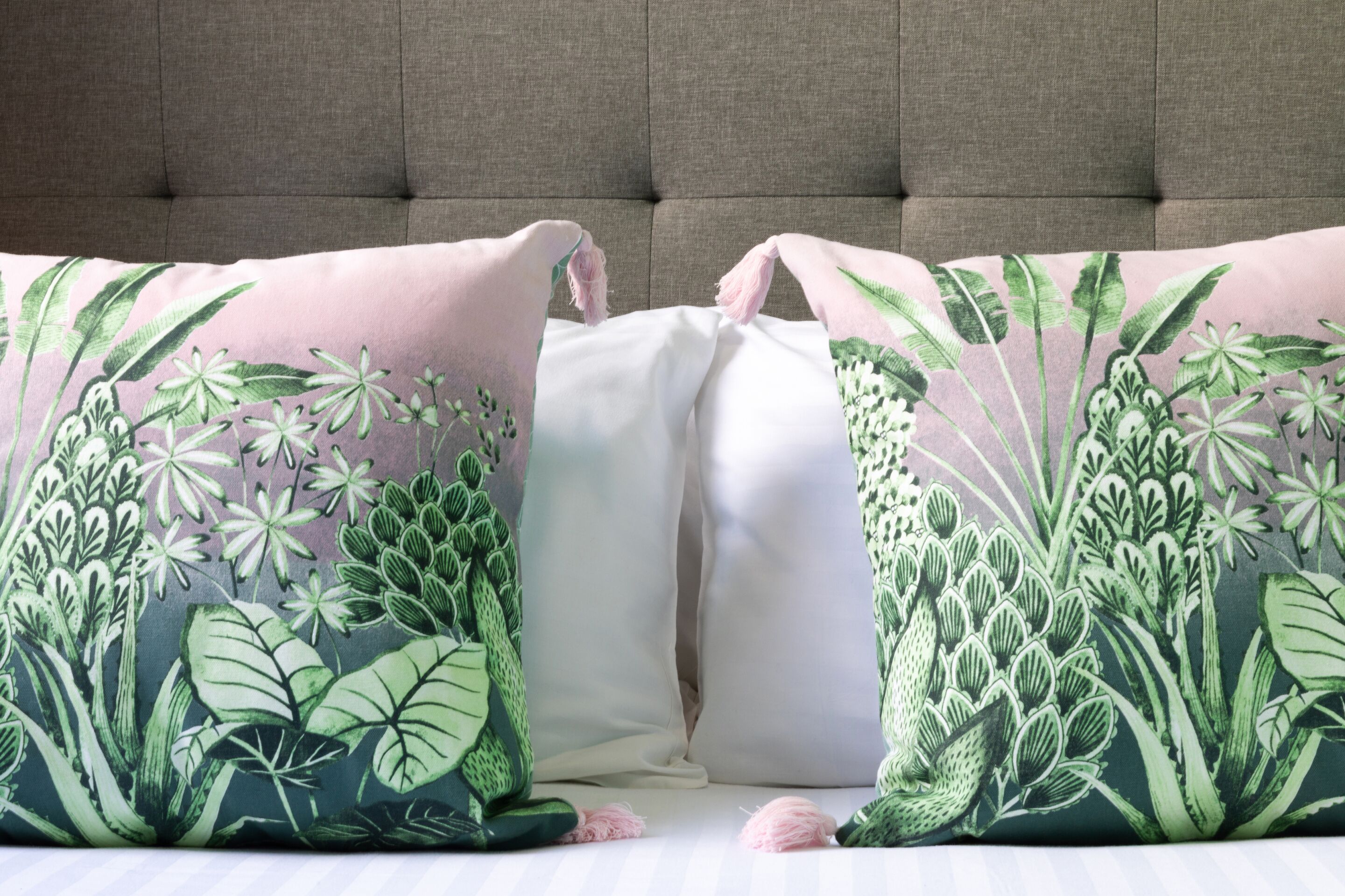A bed with two pillows featuring a green and white floral pattern.