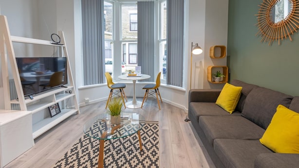 Un salon moderne doté d’un téléviseur, de sièges, d’un coin repas et de grandes fenêtres.