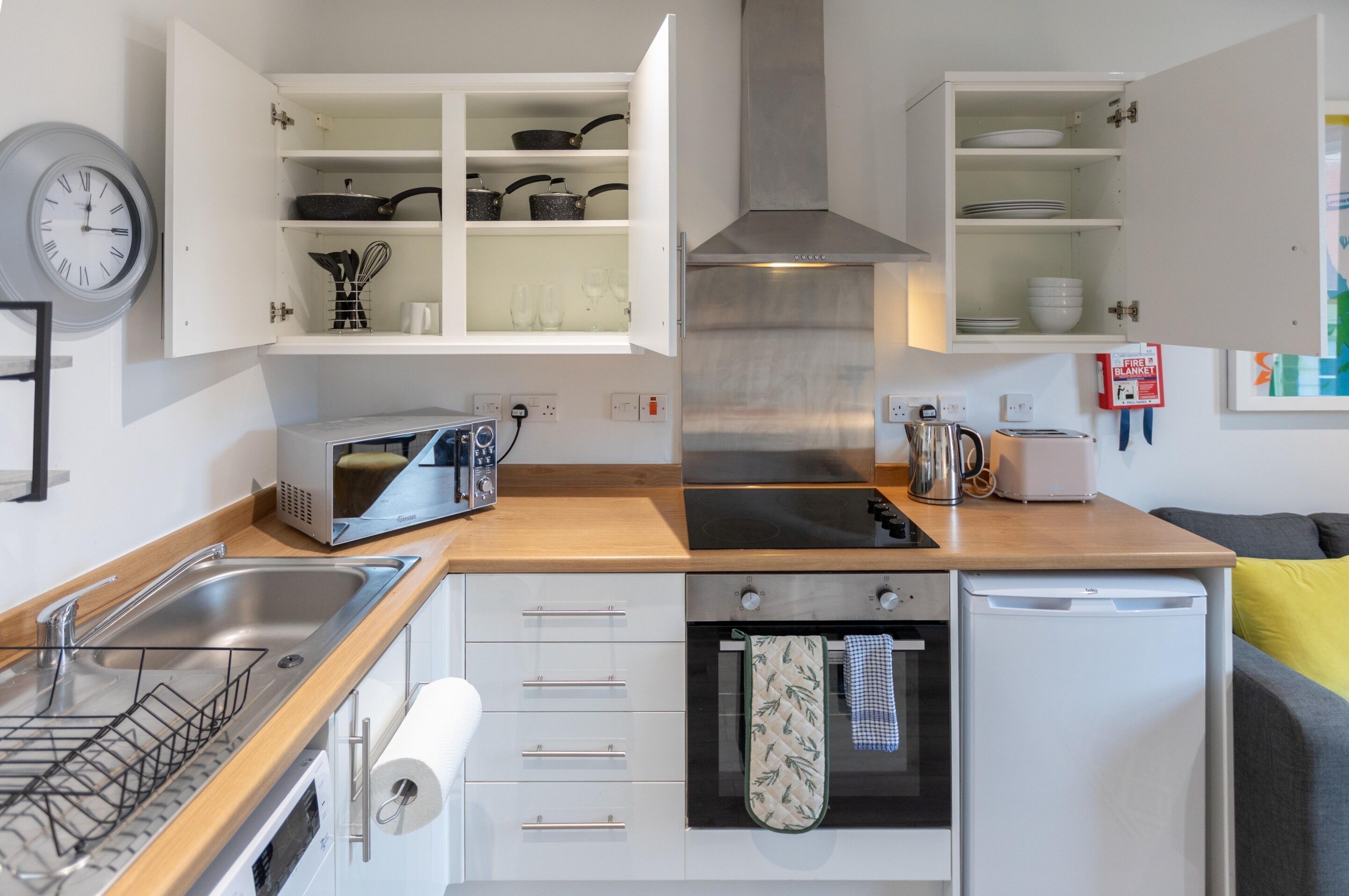 Een moderne keuken met witte kasten, een roestvrijstalen afzuigkap, een magnetron, een broodrooster en een vaatwasser.