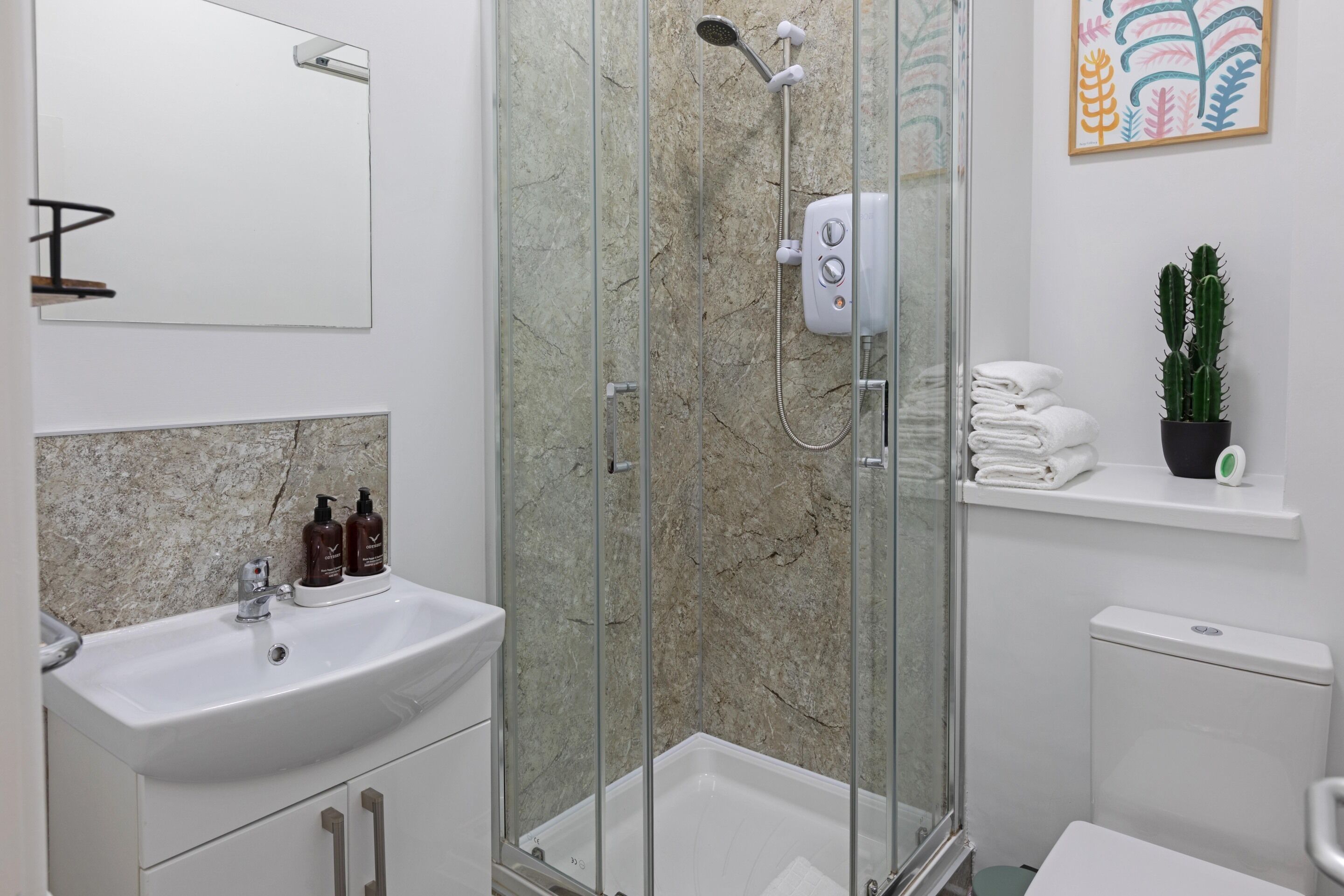 A modern bathroom with a glass-enclosed shower, a sink with toiletries, and a toilet.