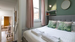 Une chambre d’hôtel avec un lit, une table de chevet, un miroir et une fenêtre avec des rideaux.
