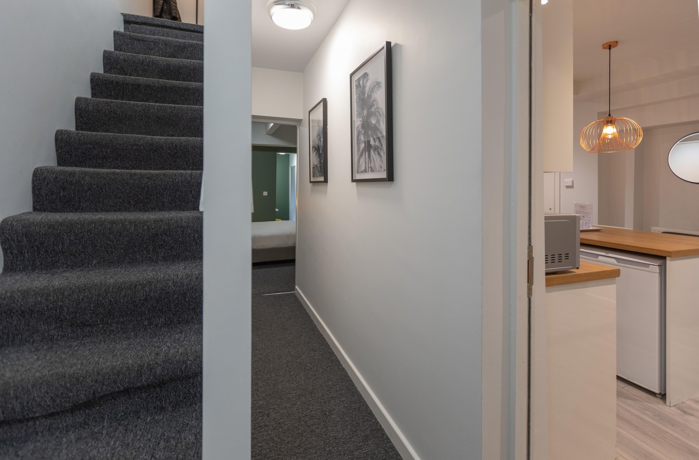 A modern interior with a carpeted staircase, a kitchen area with a microwave, and framed artwork on the wall.