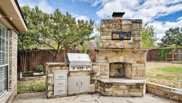 Une cheminée extérieure en pierre, dotée d’un barbecue et d’un conduit de cheminée en pierre.