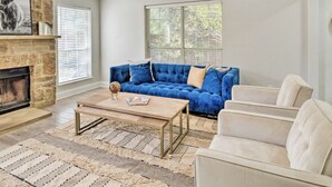 Un salon avec un canapé bleu, des fauteuils beige, une table basse et une cheminée.