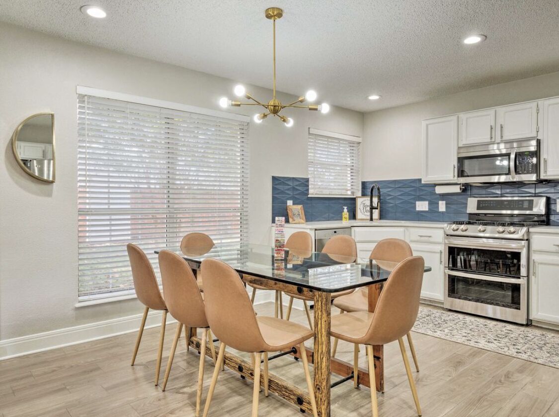 Una cucina moderna con zona pranzo, caratterizzata da un tavolo con piano in vetro, sedie color beige ed elettrodomestici in acciaio inossidabile.