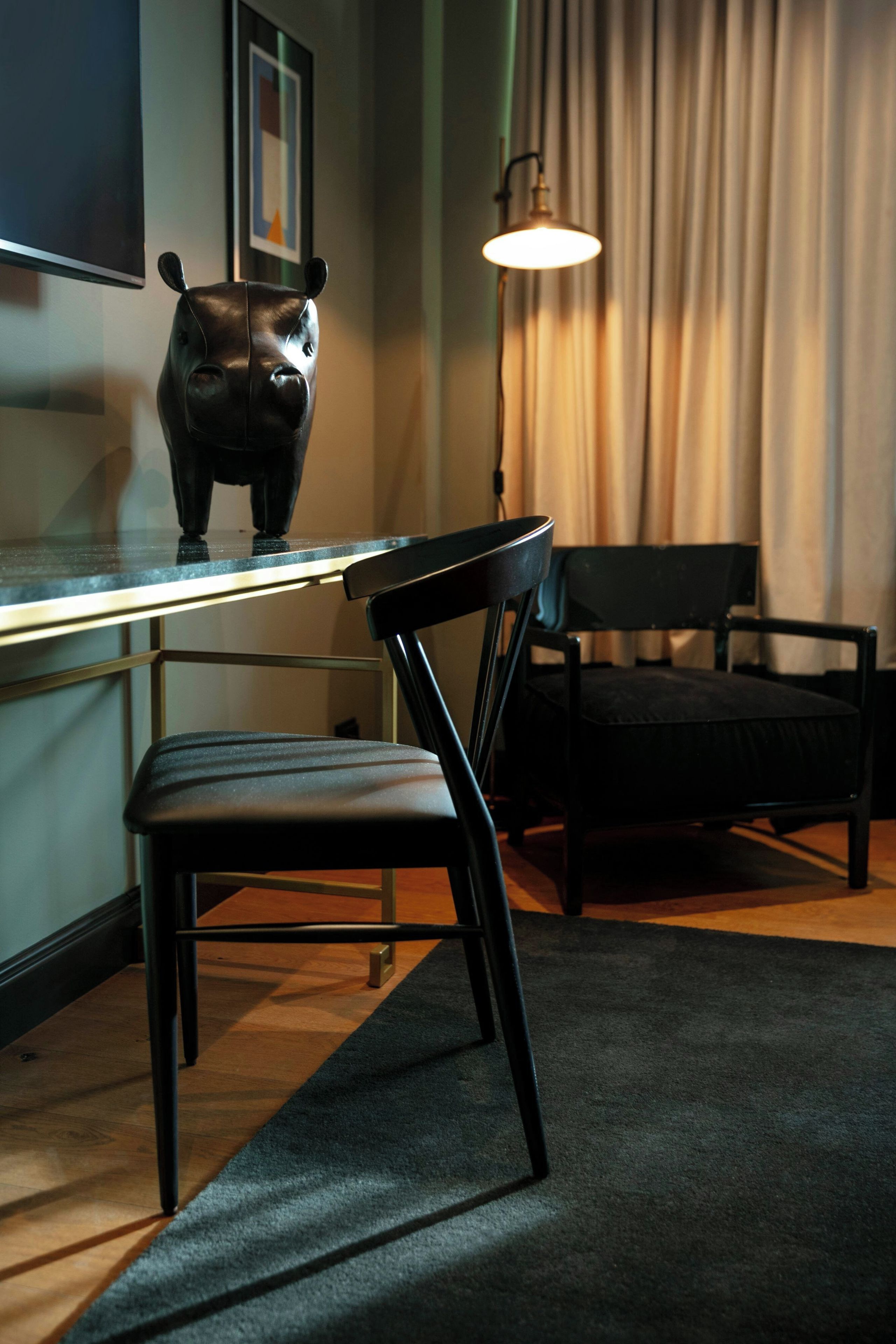 Ein stilvolles Zimmer mit Schreibtisch, Stuhl, Lampe und einer dekorativen Skulptur.