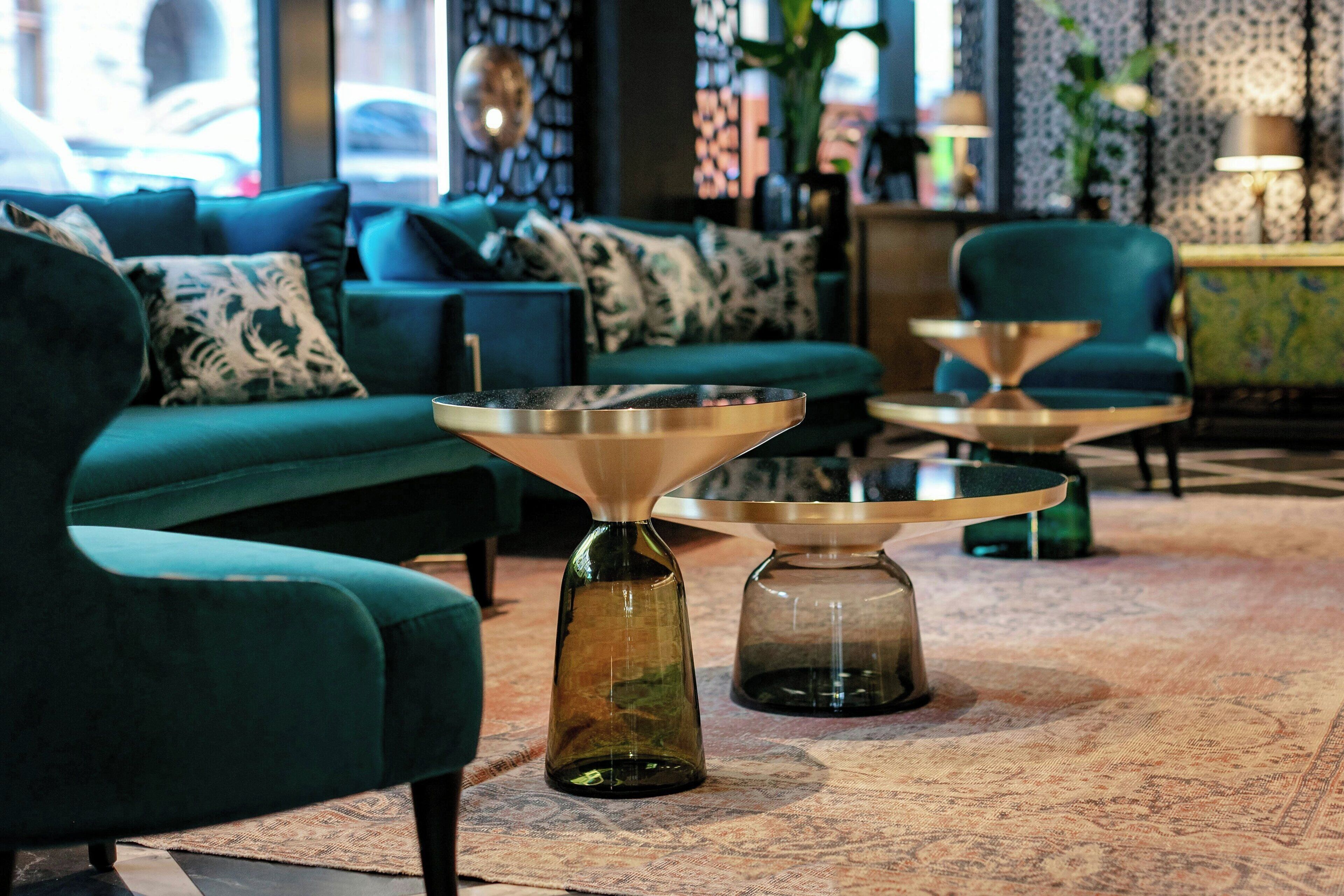 Ein modernes Wohnzimmer mit Türkis-Sofas, gemusterten Kissen und zwei Couchtischen mit Glastischplatten.
