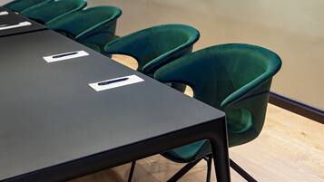 Un salón de conferencias con una larga mesa y seis sillas verdes.