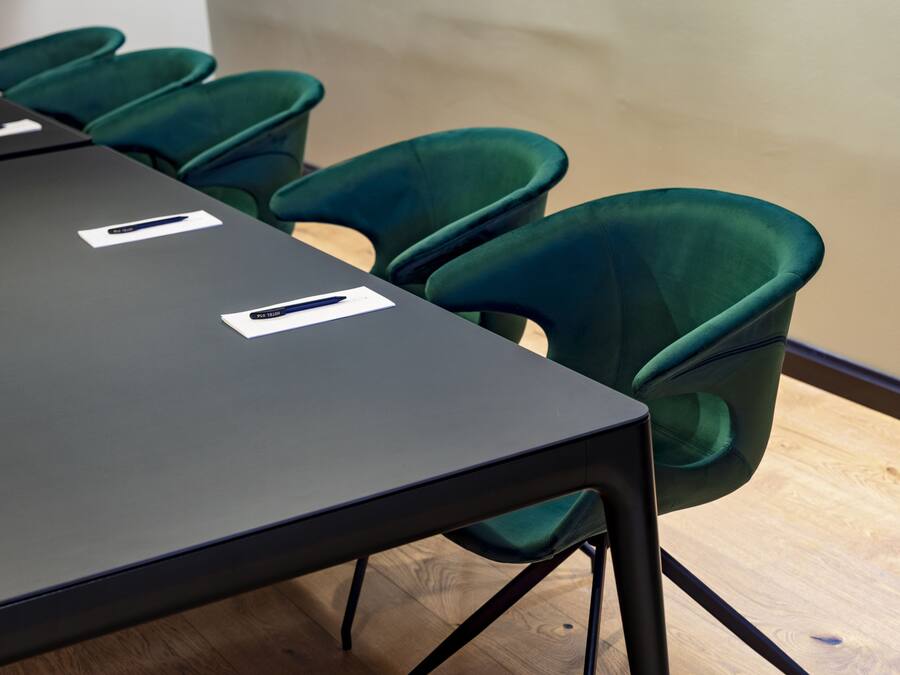 Un salón de conferencias con una larga mesa y seis sillas verdes.
