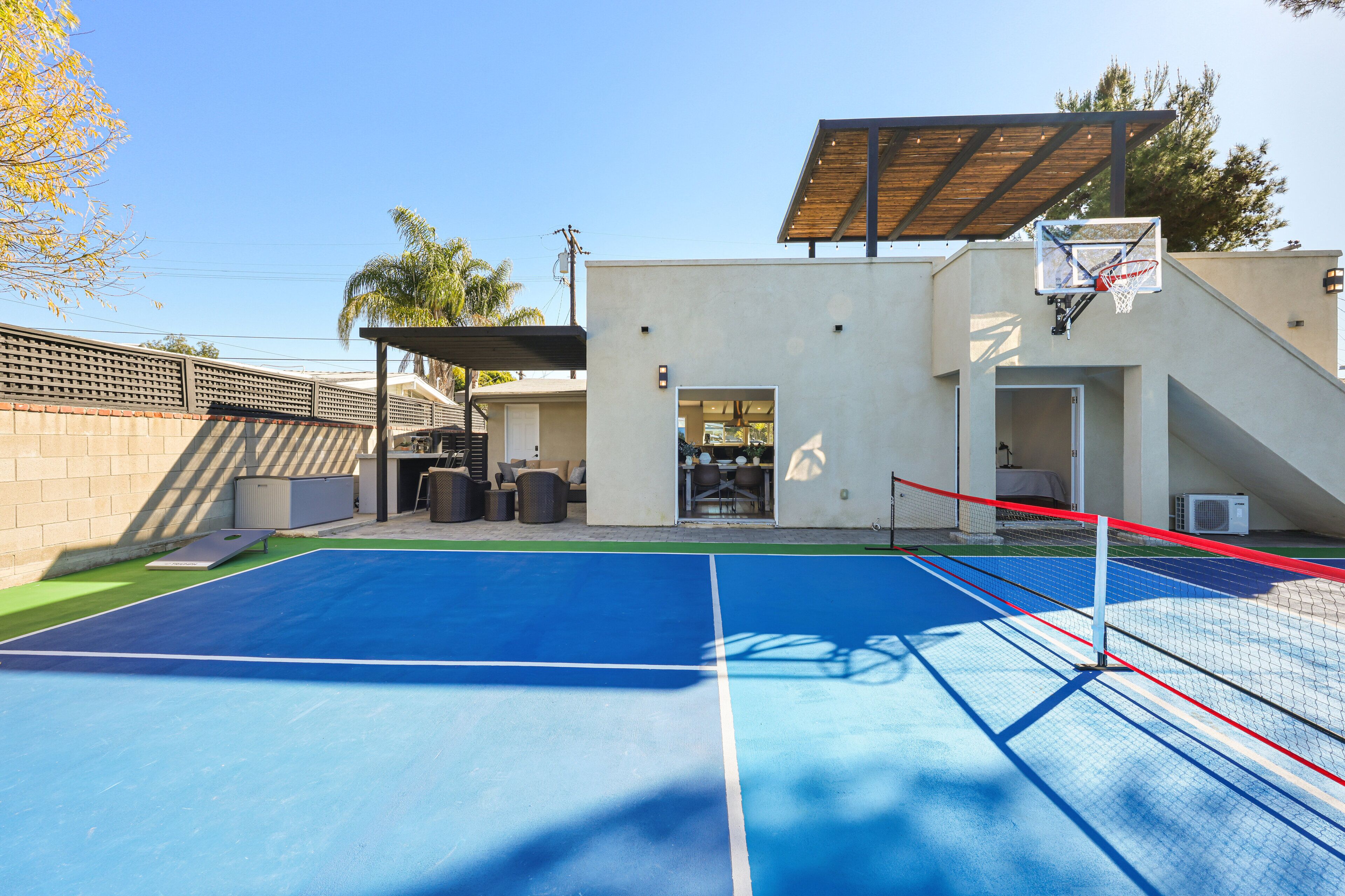 Un terrain de basket-ball en plein air, équipé d’un panier, d’un espace de repos couvert et d’un bâtiment doté d’une porte et de fenêtres.