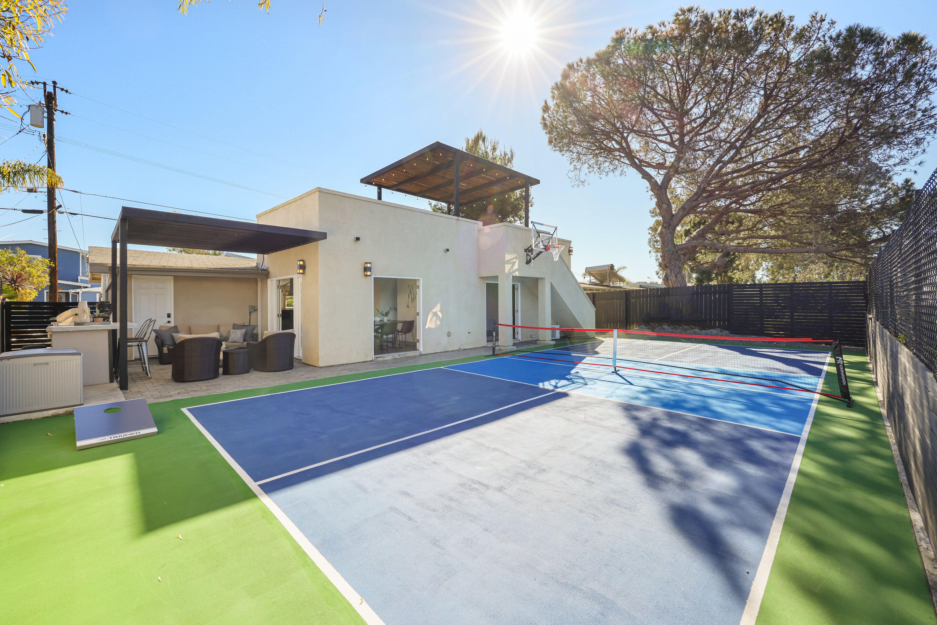 An outdoor tennis court with a covered seating area and a building in the background.