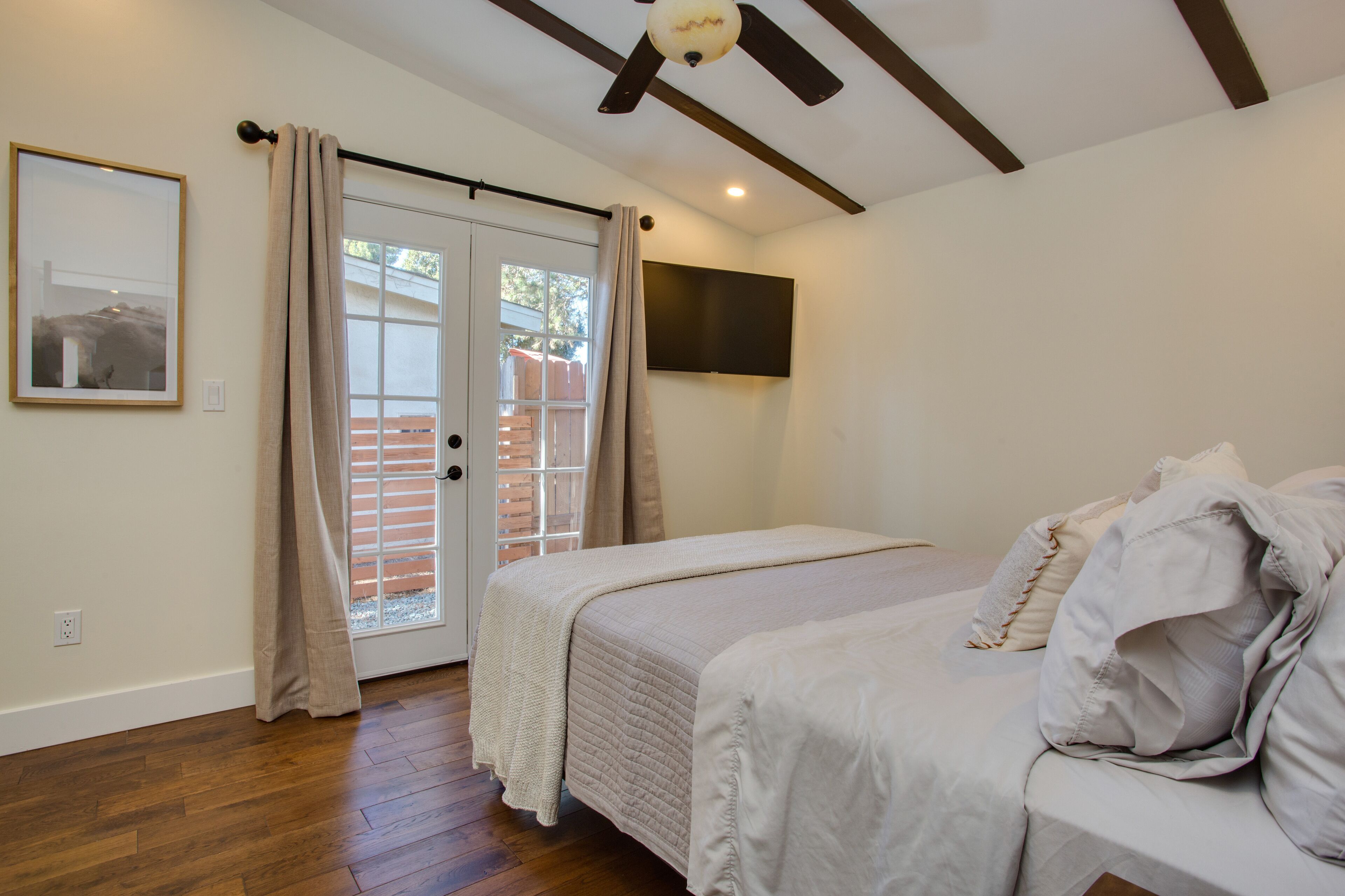 A bedroom with a bed, a television mounted on the wall, and a sliding glass door leading to an outdoor area.