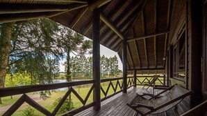 A wooden deck with a view of a lake and trees, and a covered area with a railing. - Aires de Patagônia Pousada (Cambara do Sul)