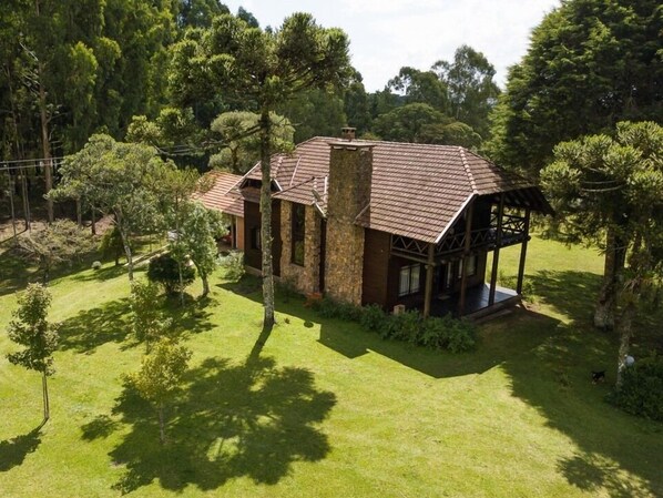 A two-story stone house with a large chimney, surrounded by a well-maintained lawn and trees. - Aires de Patagônia Pousada (Cambara do Sul)