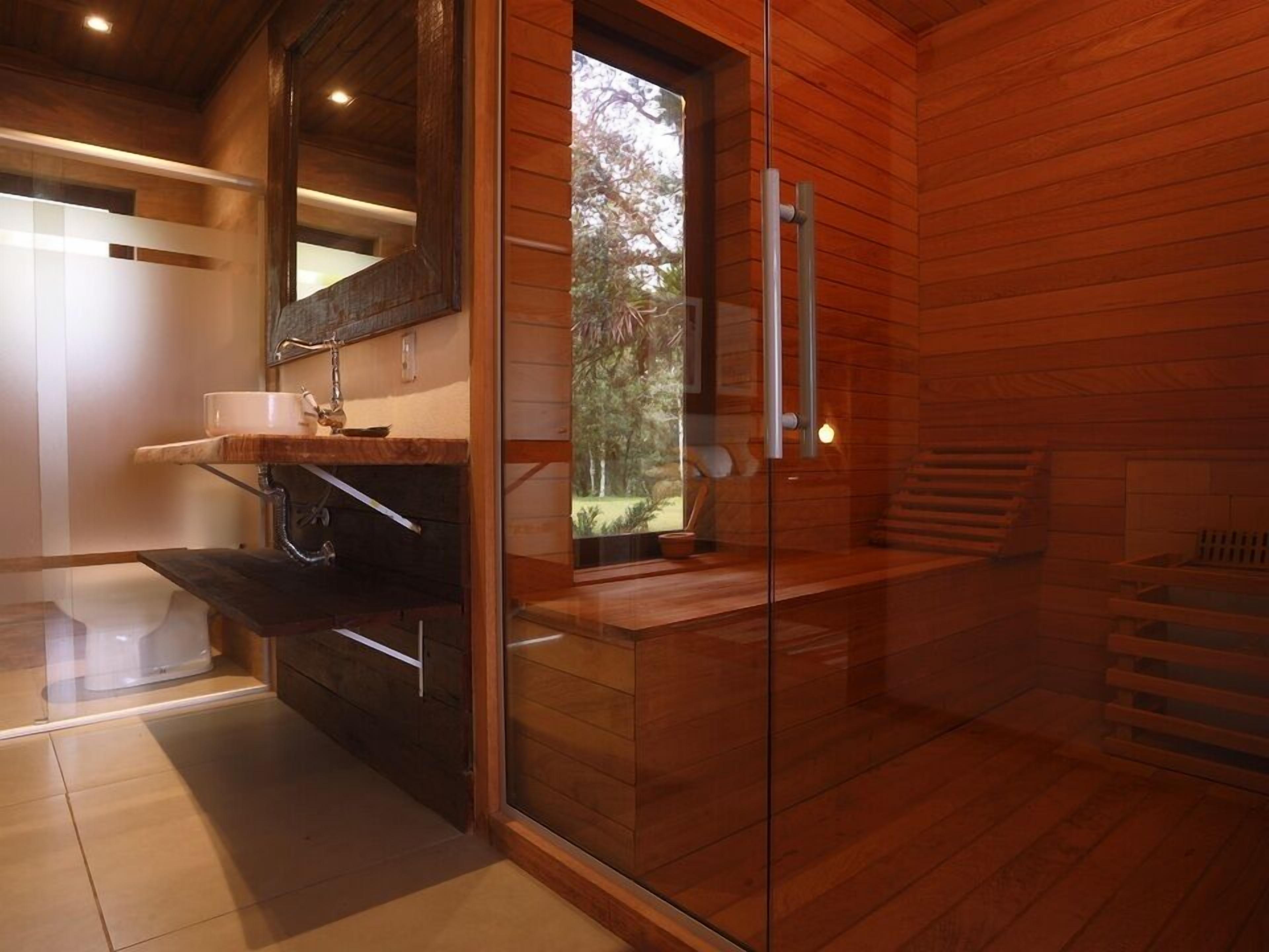 A modern bathroom with a glass shower enclosure, wooden interior, and a view of the outdoors.