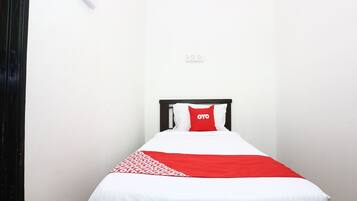 A single bed with a white and red bedspread, a black headboard, and a red pillow with the word "OYO" on it.