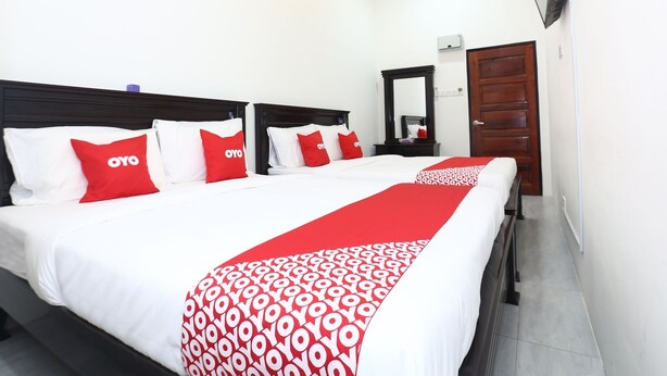 Habitación de hotel con dos camas, cada una con ropa de cama blanca y almohadas rojas, un corredor de cama con estampado rojo y blanco, un cabecero de madera, un espejo y una puerta de madera.