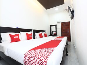 Habitación de hotel con dos camas, cada una con ropa de cama blanca y almohadas rojas, un corredor de cama con estampado rojo y blanco, un cabecero de madera, un espejo y una puerta de madera.