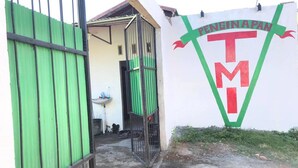 Un bâtiment avec une porte verte, un mur blanc orné d’un logo et une petite fenêtre.