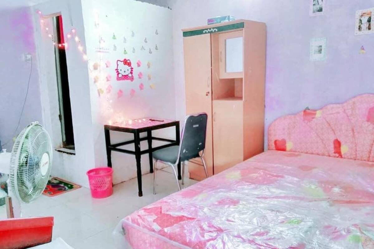 Une chambre à coucher comprenant un lit, un bureau, une chaise, une armoire et un ventilateur.