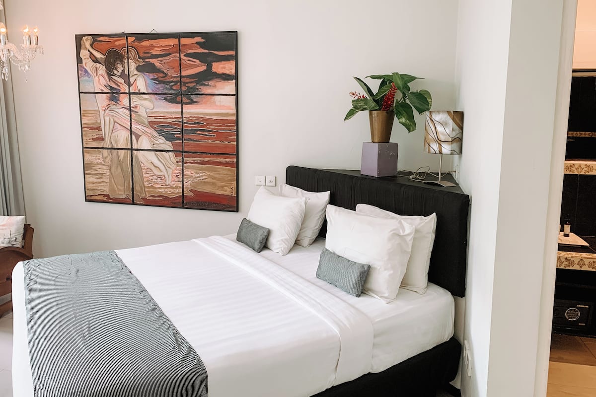 A neatly made bed with white bedding and a striped throw, a black headboard, and a large abstract painting on the wall.