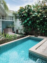 Uma piscina retangular com água azul cristalina, rodeada por uma borda de azulejos e uma faixa de pedras.