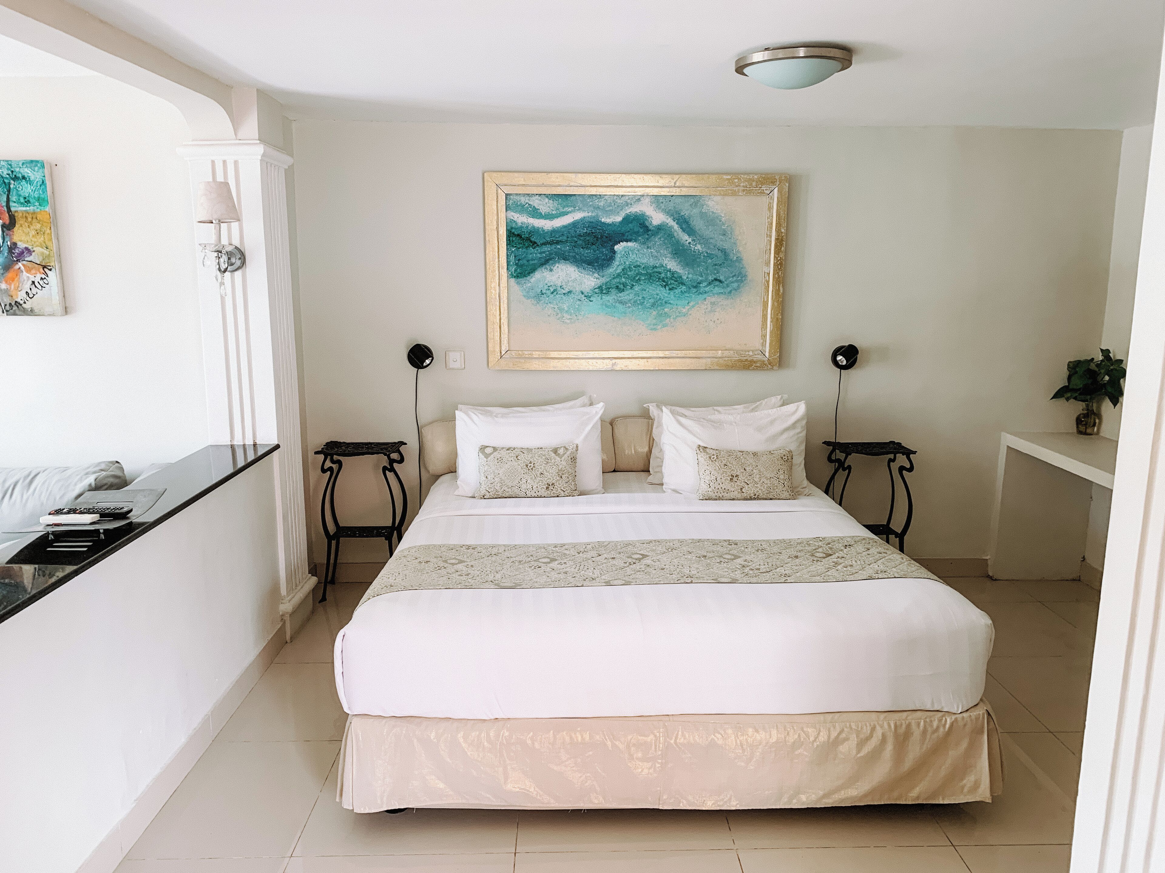 A neatly arranged bedroom with a large bed, bedside tables, and a painting on the wall.