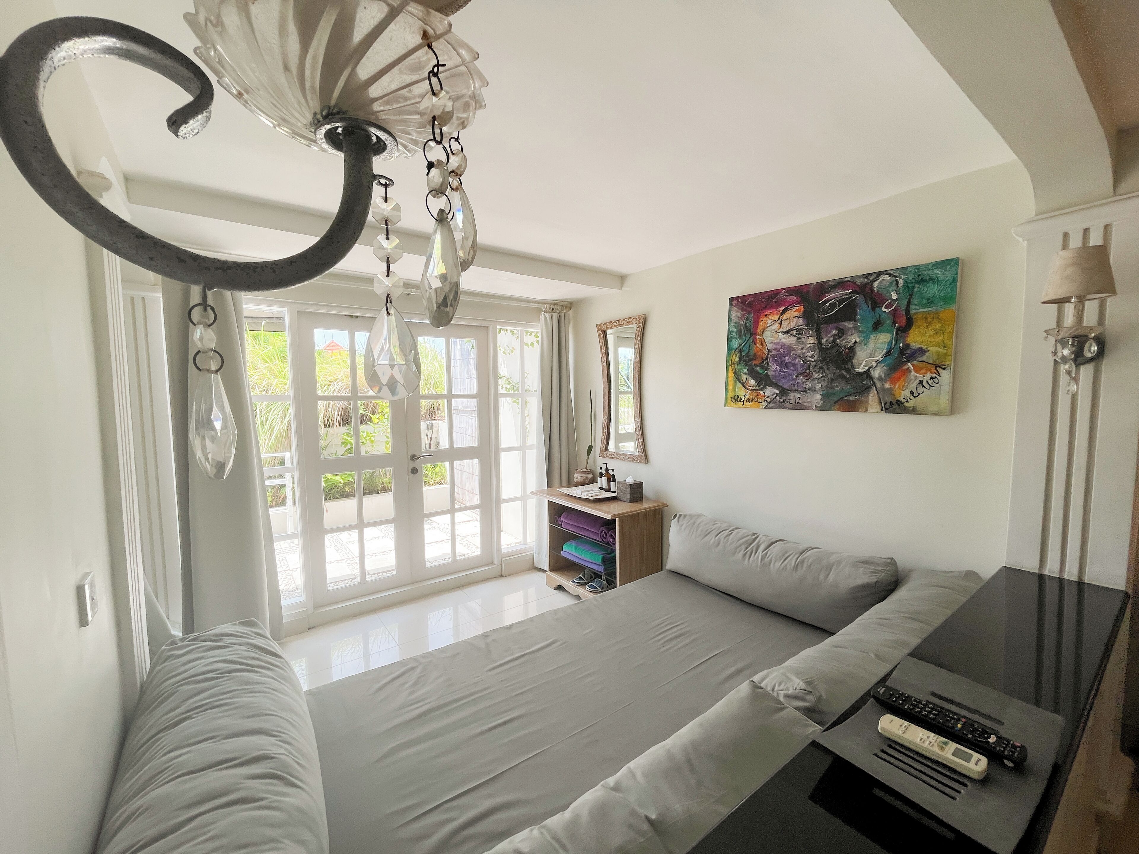 Une chambre à coucher avec un lit, une table de chevet avec une lampe, un tableau au mur et une fenêtre avec des rideaux.
