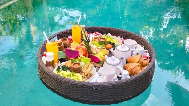 A poolside breakfast setup with a wicker tray containing food and drinks. - Casa Artista By Villa Kresna (Seminyak)