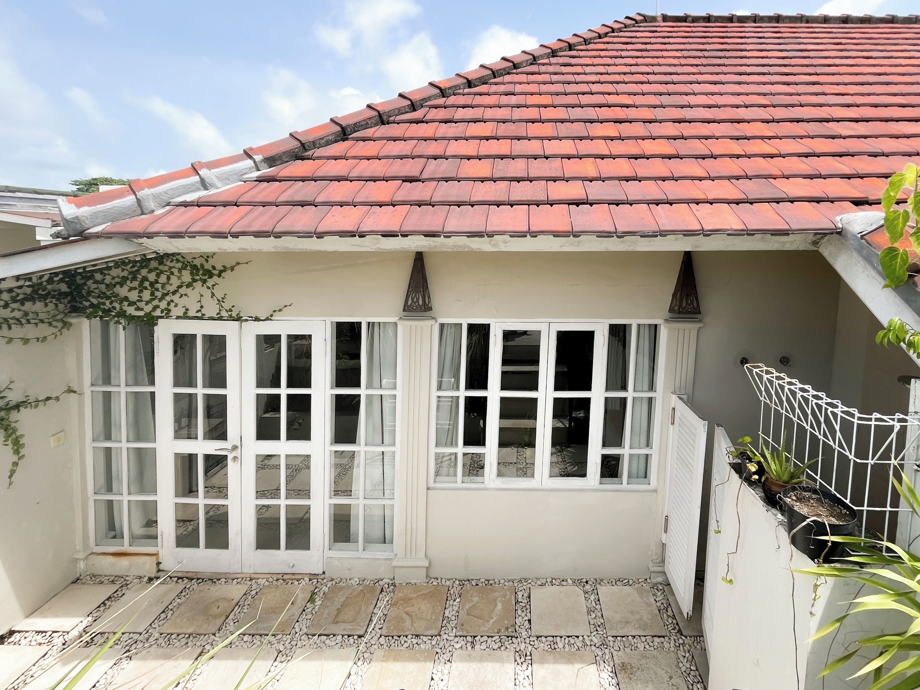 Uma casa com telhado de telhas vermelhas, janelas emolduradas de branco e um pátio com piso de pedra.