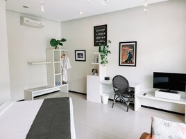 Quarto de hotel moderno com cama, escrivaninha, cadeira, televisão e estante de livros.