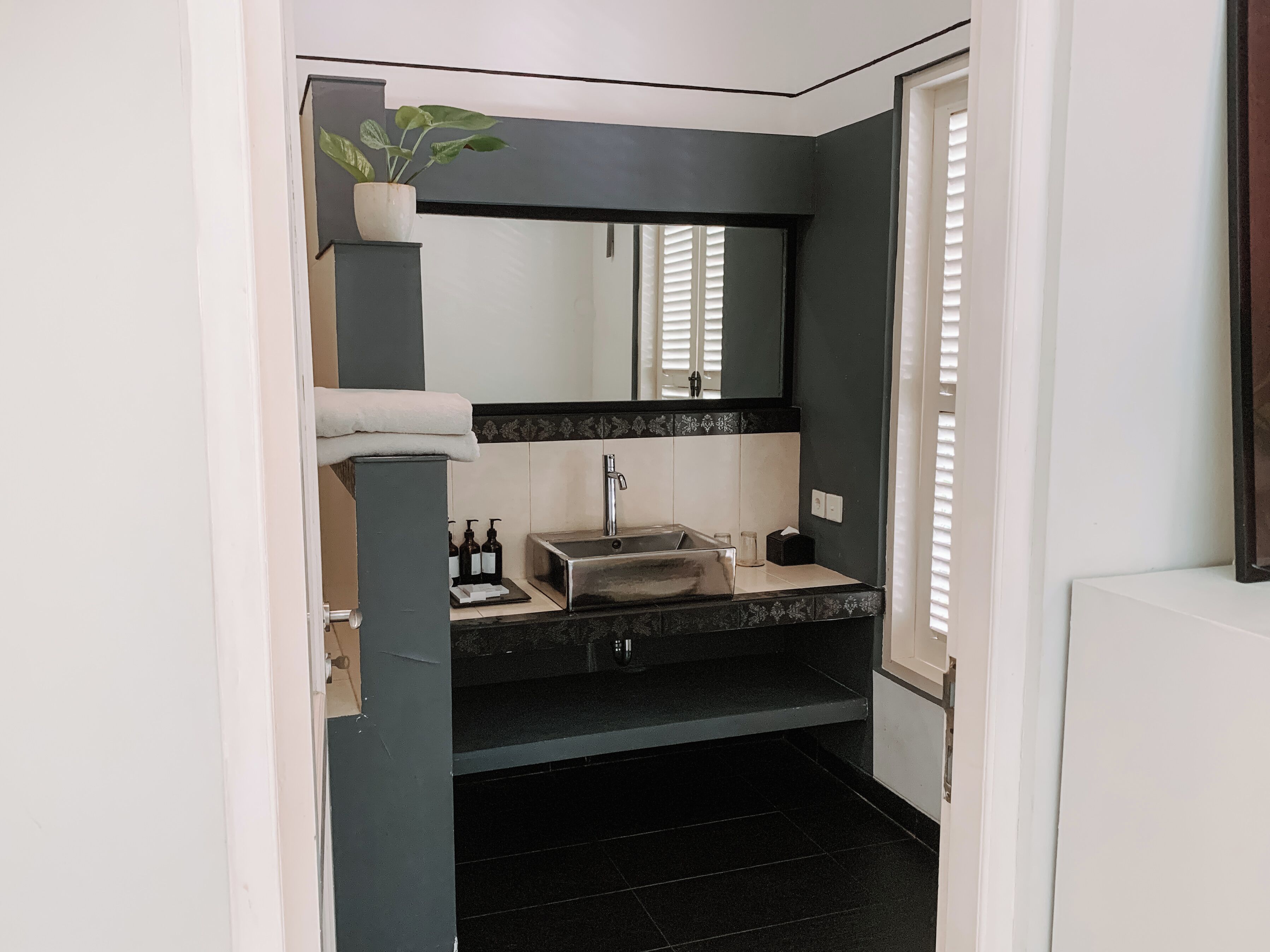 A modern bathroom with a black and white color scheme, featuring a sink, mirror, and a potted plant.