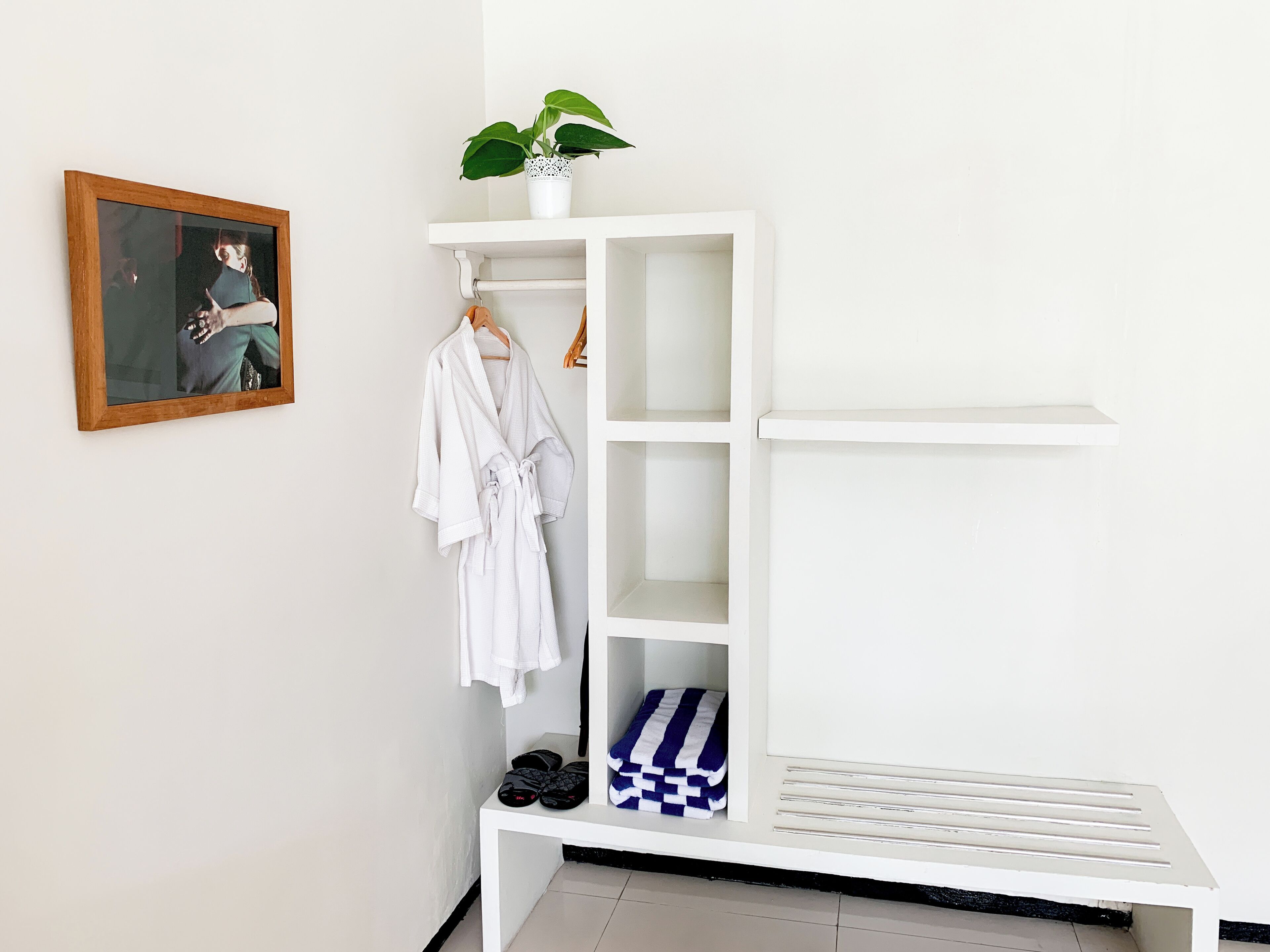 Un armario blanco con varios estantes, una percha y un banco con zapatos y toallas.