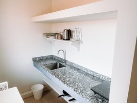 A kitchen with a granite countertop, a stainless steel sink, and a built-in oven. There are shelves above the sink holding kitchenware and a trash bin to the left.