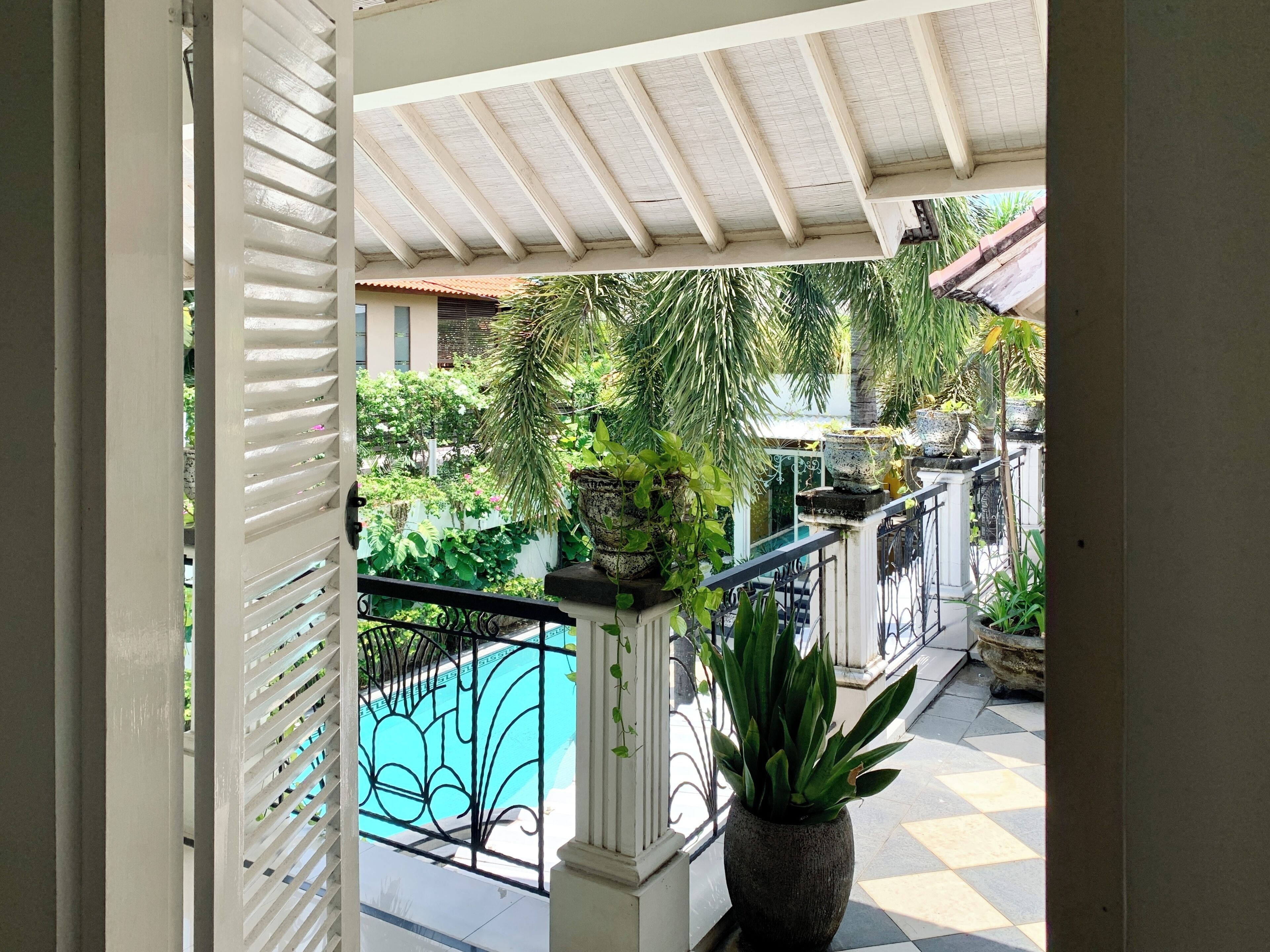 A balcony with a view of a swimming pool, surrounded by potted plants and a tiled floor.