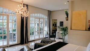 A spacious bedroom with a large bed, a chandelier, and a view of the outdoors through large windows. - Casa Artista By Villa Kresna (Seminyak)