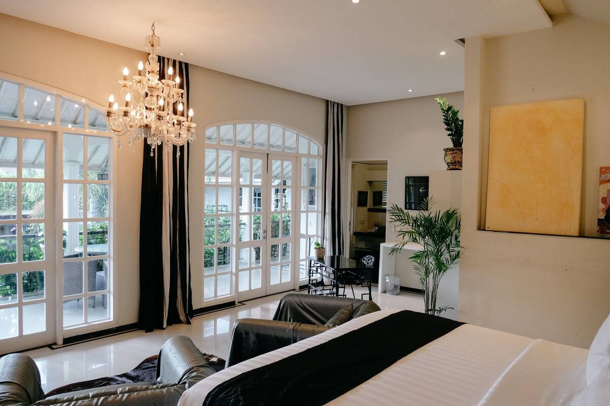 A spacious bedroom with a large bed, a chandelier, and a view of the outdoors through large windows.