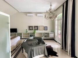 Uma sala de estar moderna com um sofá, uma televisão, um candelabro e uma janela grande com cortinas.