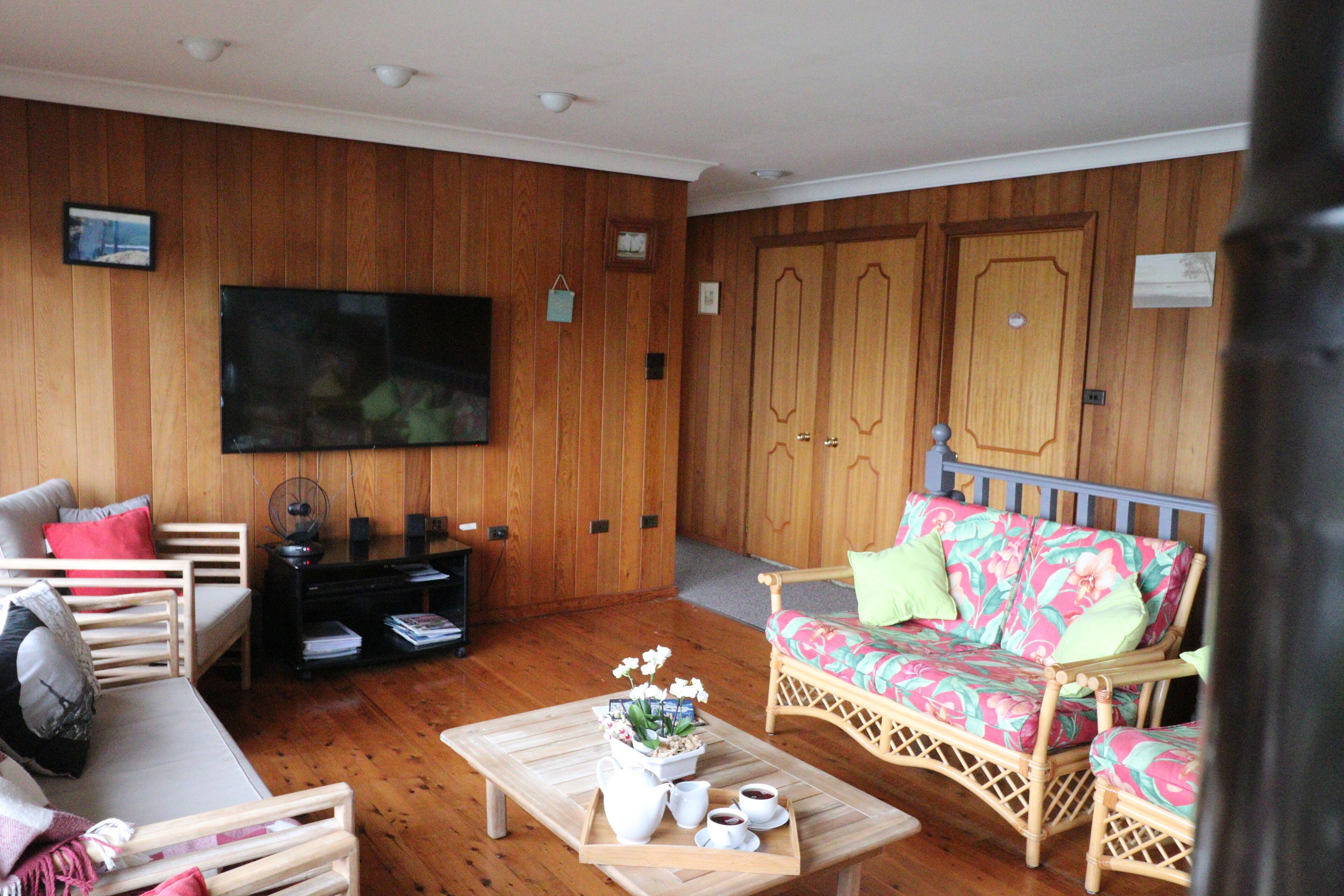 A cozy living room with a television, wicker furniture, a wooden floor, and a large wooden door.