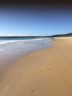 A wide sandy beach with gentle waves and a clear sky.