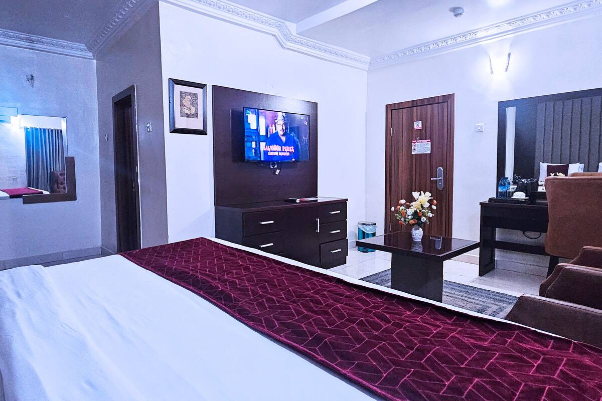 A hotel room with a large bed, a TV, a desk with a chair, and a mirror.