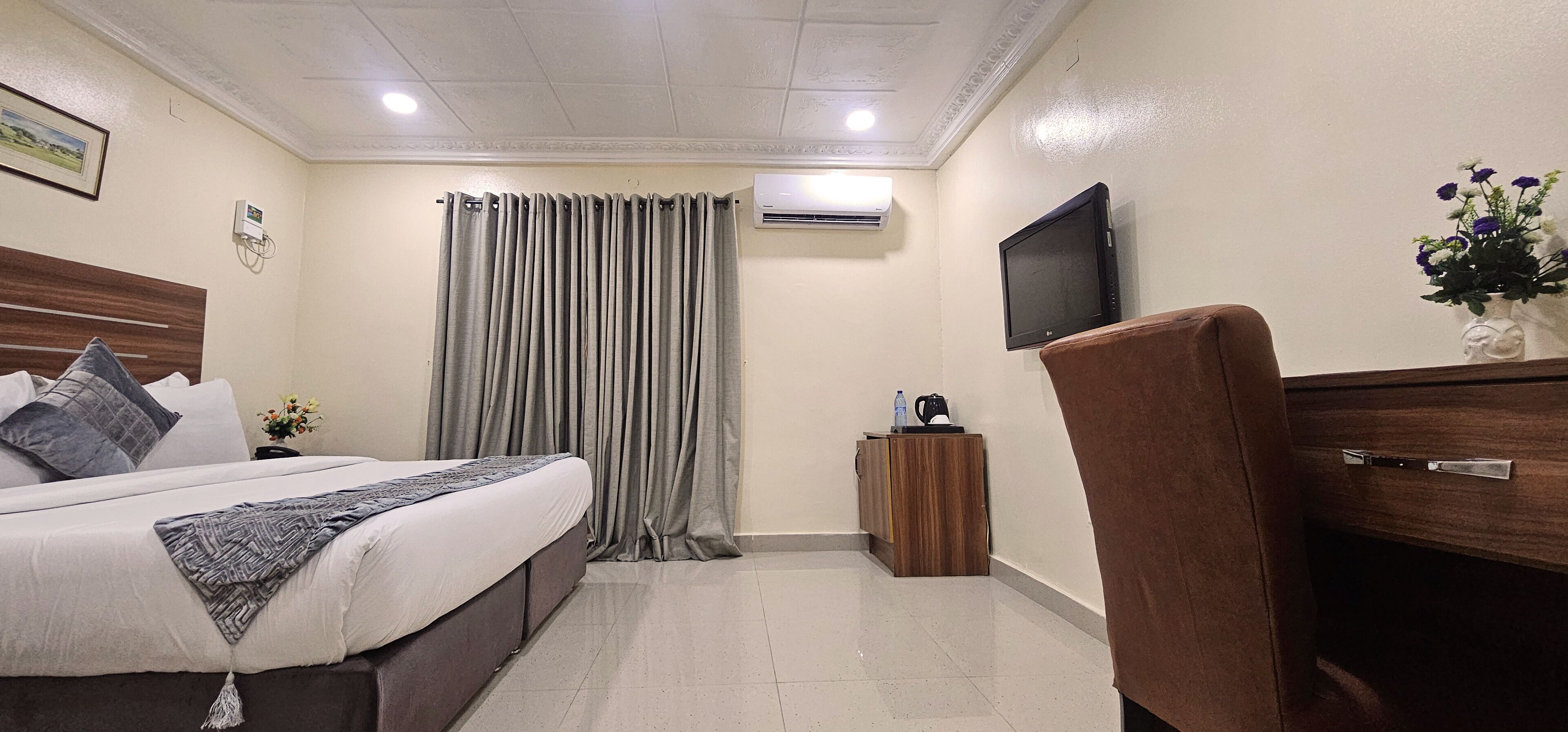 A hotel room with a bed, a TV, a small cabinet, and a curtain.