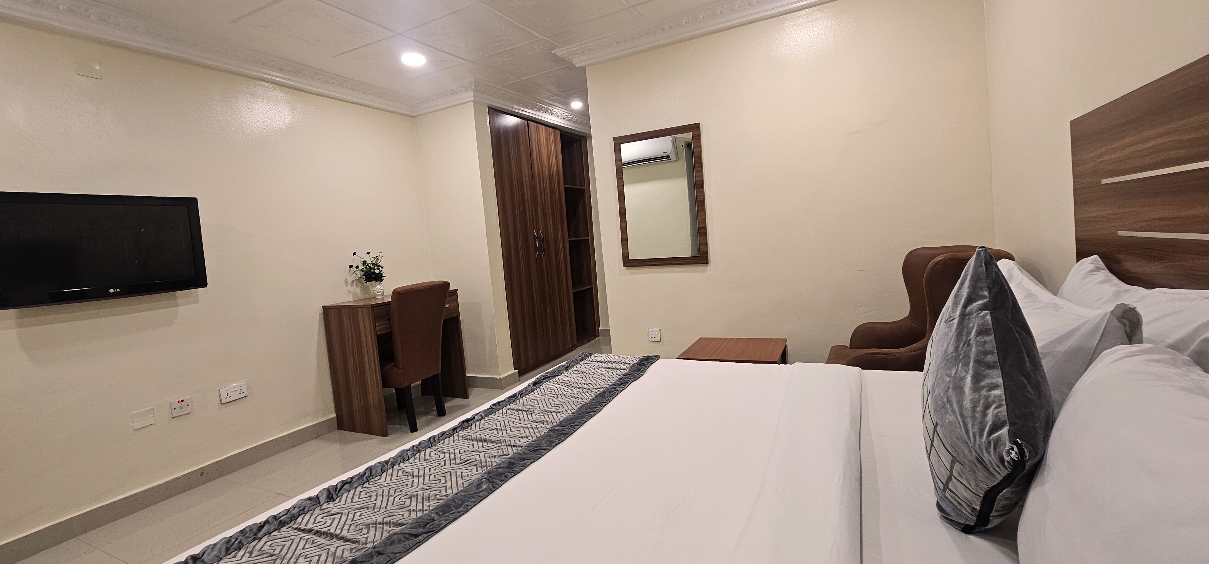 Une chambre d’hôtel équipée d’un lit, d’une télévision, d’une armoire, d’un bureau et d’un miroir.